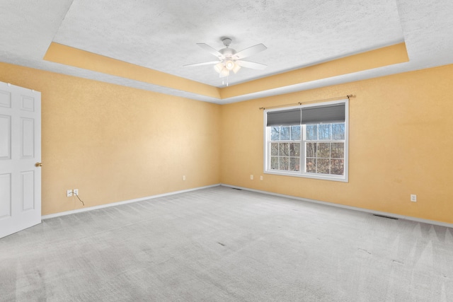 unfurnished room with a tray ceiling, carpet floors, a textured ceiling, and baseboards