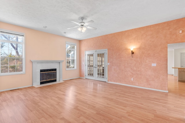 unfurnished living room with a fireplace with flush hearth, french doors, light wood-type flooring, and ceiling fan