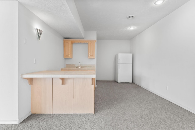 kitchen featuring light carpet, light brown cabinetry, a kitchen breakfast bar, freestanding refrigerator, and tile countertops