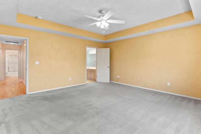 unfurnished room with a tray ceiling, light colored carpet, baseboards, and ceiling fan