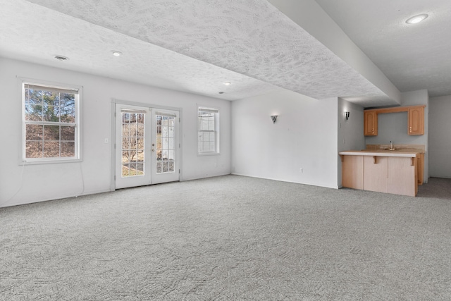 unfurnished living room with recessed lighting, a sink, french doors, a textured ceiling, and light colored carpet