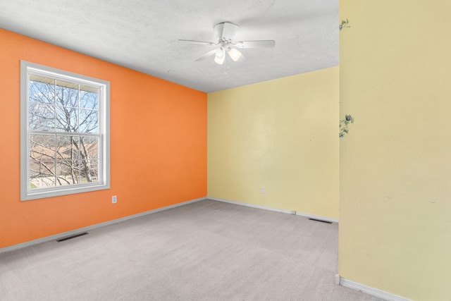 carpeted spare room featuring visible vents, a textured ceiling, and ceiling fan