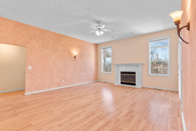 unfurnished living room featuring light wood finished floors, plenty of natural light, ceiling fan, and a fireplace with flush hearth