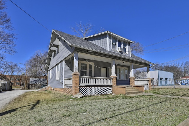 bungalow-style home with covered porch, a shingled roof, a front yard, and fence