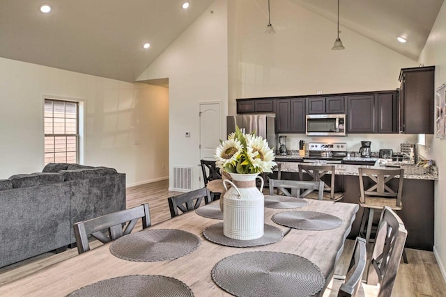 dining area with visible vents, baseboards, high vaulted ceiling, and light wood finished floors