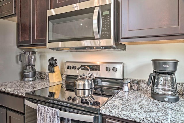 kitchen featuring light stone counters, stainless steel appliances, dark brown cabinets, and wood finished floors