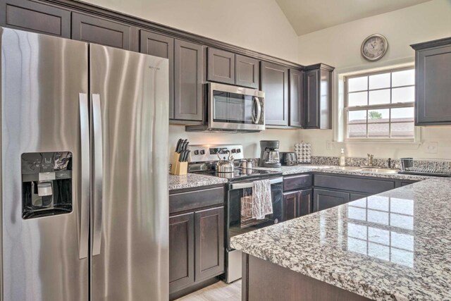 kitchen featuring lofted ceiling, light stone countertops, and appliances with stainless steel finishes