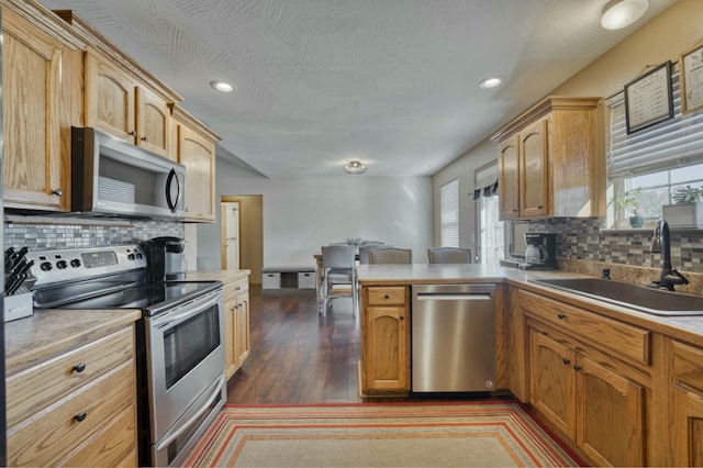 kitchen with a sink, appliances with stainless steel finishes, a peninsula, light countertops, and dark wood-style flooring