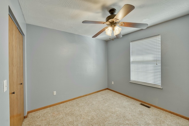 carpeted empty room featuring visible vents, baseboards, and a ceiling fan