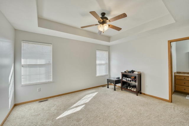 carpeted empty room with a raised ceiling, baseboards, visible vents, and ceiling fan