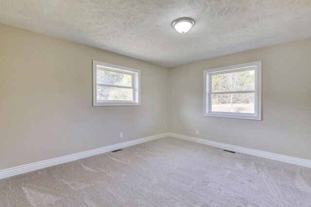 unfurnished room featuring baseboards, plenty of natural light, light colored carpet, and visible vents