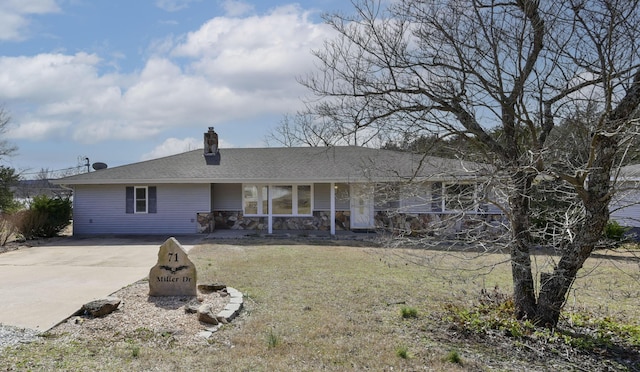 rear view of property with a yard, concrete driveway, a chimney, and a shingled roof