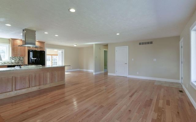 kitchen featuring visible vents, island range hood, light wood-type flooring, decorative backsplash, and black refrigerator with ice dispenser