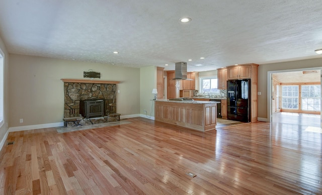 kitchen featuring island exhaust hood, light wood-style floors, a peninsula, black refrigerator with ice dispenser, and stainless steel gas cooktop