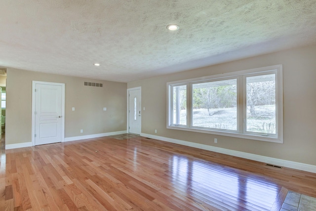 interior space with visible vents, light wood-style flooring, a textured ceiling, and baseboards