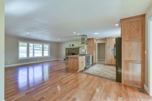 kitchen with open floor plan, gas range, light wood-type flooring, a stone fireplace, and freestanding refrigerator