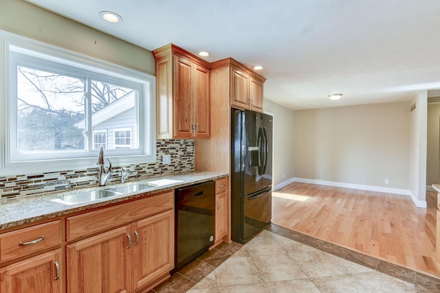 kitchen with black appliances, a sink, light stone counters, decorative backsplash, and baseboards