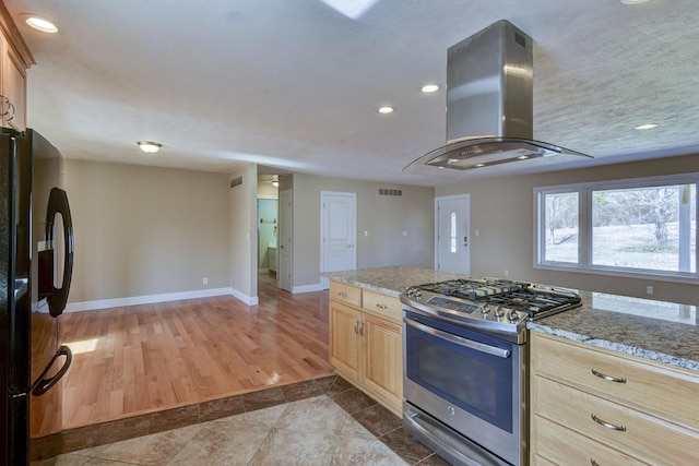 kitchen featuring visible vents, island exhaust hood, light brown cabinetry, gas range, and black fridge