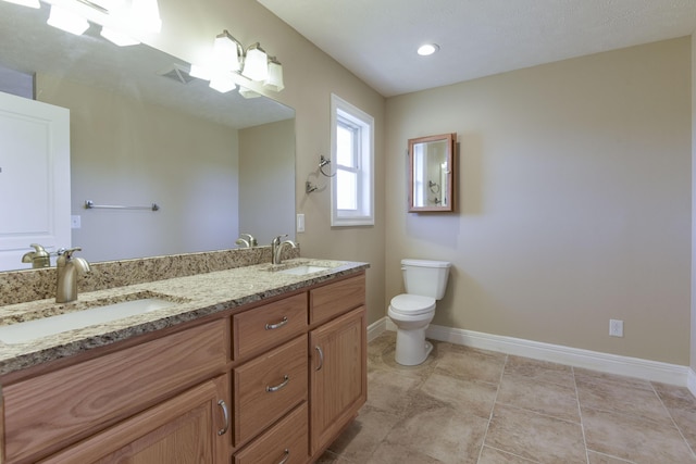 bathroom with a sink, baseboards, toilet, and double vanity