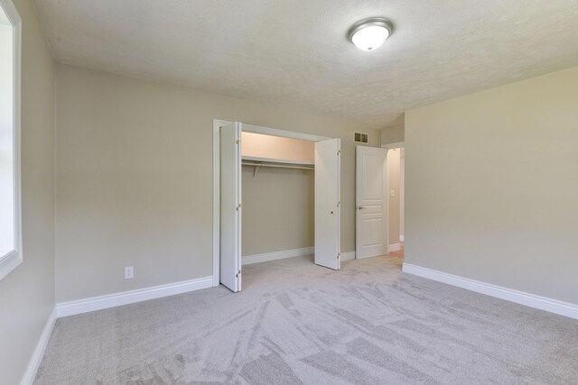 unfurnished bedroom with light colored carpet, baseboards, visible vents, and a textured ceiling