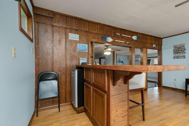 bar featuring crown molding, baseboards, ceiling fan, wood walls, and light wood-style flooring