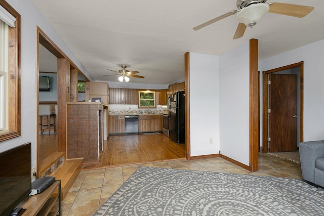 kitchen with baseboards, dishwashing machine, freestanding refrigerator, brown cabinetry, and a sink