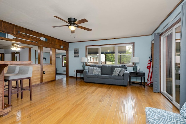 living area with baseboards, a ceiling fan, light wood-type flooring, and ornamental molding