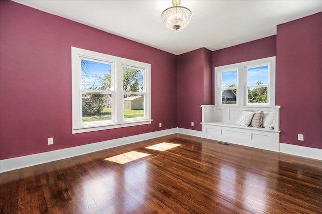 empty room with visible vents, plenty of natural light, baseboards, and wood finished floors