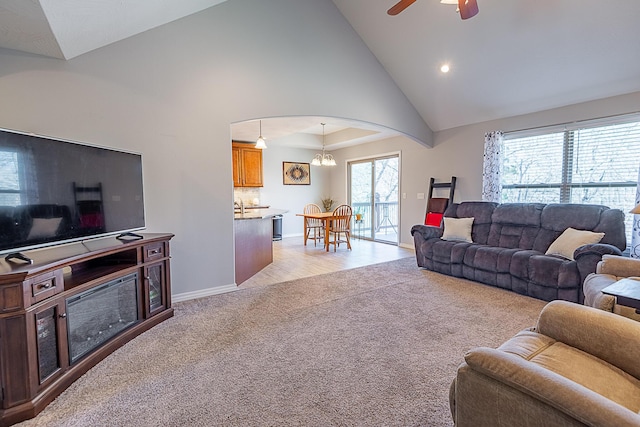 living room featuring a ceiling fan, baseboards, high vaulted ceiling, arched walkways, and light colored carpet