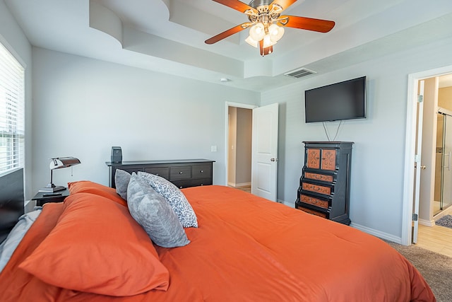 carpeted bedroom with a ceiling fan, a tray ceiling, baseboards, and visible vents