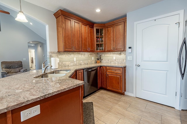 kitchen featuring brown cabinetry, light stone countertops, dishwasher, arched walkways, and a sink