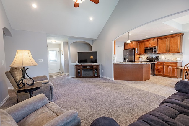 living room with baseboards, ceiling fan, light colored carpet, arched walkways, and high vaulted ceiling