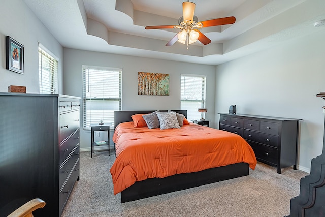 bedroom featuring a ceiling fan, a tray ceiling, light colored carpet, and baseboards