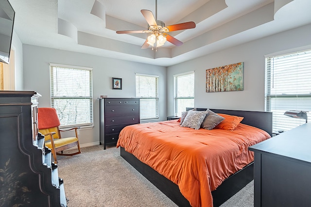 bedroom with light colored carpet, a raised ceiling, baseboards, and multiple windows