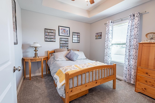 carpeted bedroom featuring a tray ceiling, a ceiling fan, and baseboards