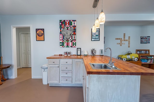 kitchen featuring a sink, finished concrete floors, a peninsula, butcher block counters, and hanging light fixtures