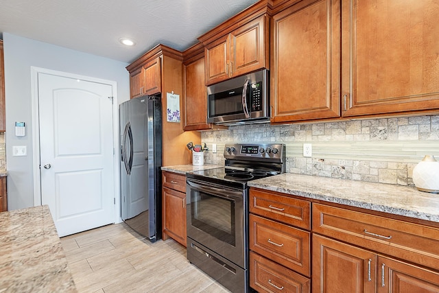 kitchen with light wood-type flooring, light stone counters, backsplash, stainless steel appliances, and brown cabinetry