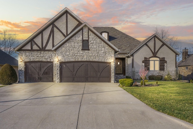 tudor house featuring stucco siding, a front lawn, concrete driveway, a shingled roof, and a garage