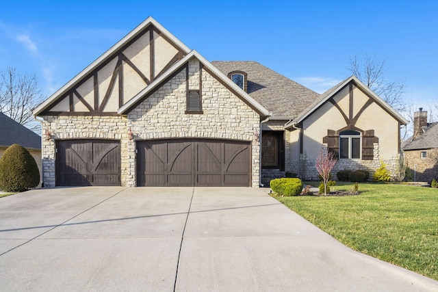 tudor-style house with stucco siding, driveway, a front lawn, roof with shingles, and a garage