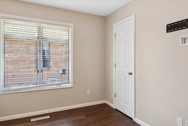 spare room featuring a wealth of natural light, visible vents, baseboards, and dark wood-style flooring