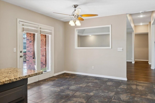 unfurnished dining area featuring stone finish flooring, baseboards, and a ceiling fan