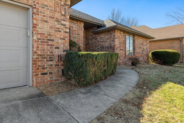 view of exterior entry with a garage, brick siding, and roof with shingles