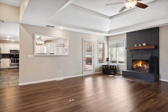 unfurnished living room featuring a tray ceiling, visible vents, dark wood finished floors, and a ceiling fan