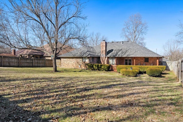 back of house featuring brick siding, a fenced backyard, a chimney, and a yard