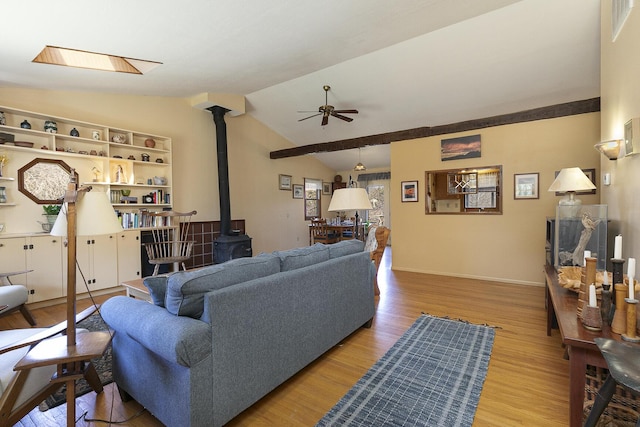 living area featuring ceiling fan, baseboards, lofted ceiling, a wood stove, and wood finished floors