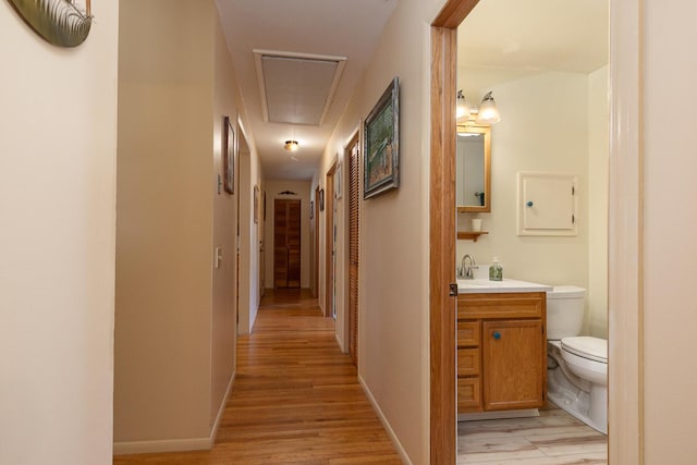 corridor featuring light wood-type flooring, baseboards, and attic access