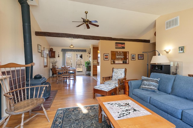 living room with visible vents, ceiling fan, lofted ceiling, a wood stove, and light wood-style floors