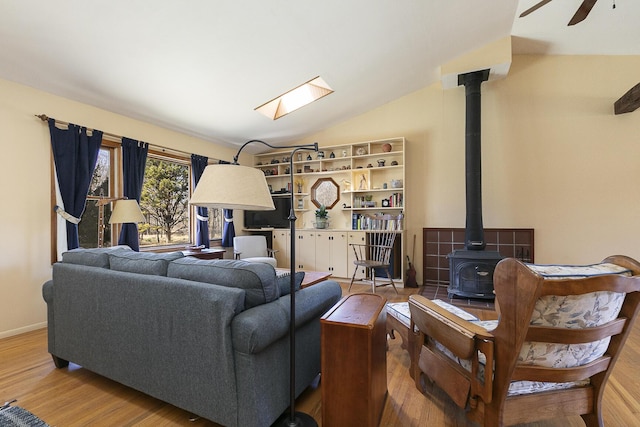 living room featuring baseboards, ceiling fan, vaulted ceiling, a wood stove, and wood finished floors