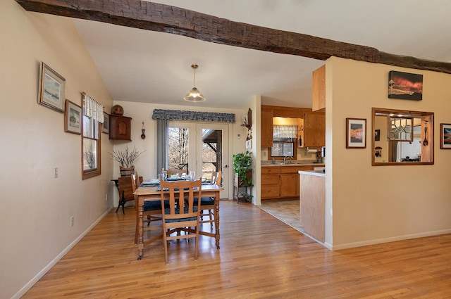 dining area with baseboards, lofted ceiling with beams, and light wood-style floors