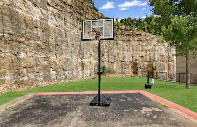 view of basketball court with a lawn and fence